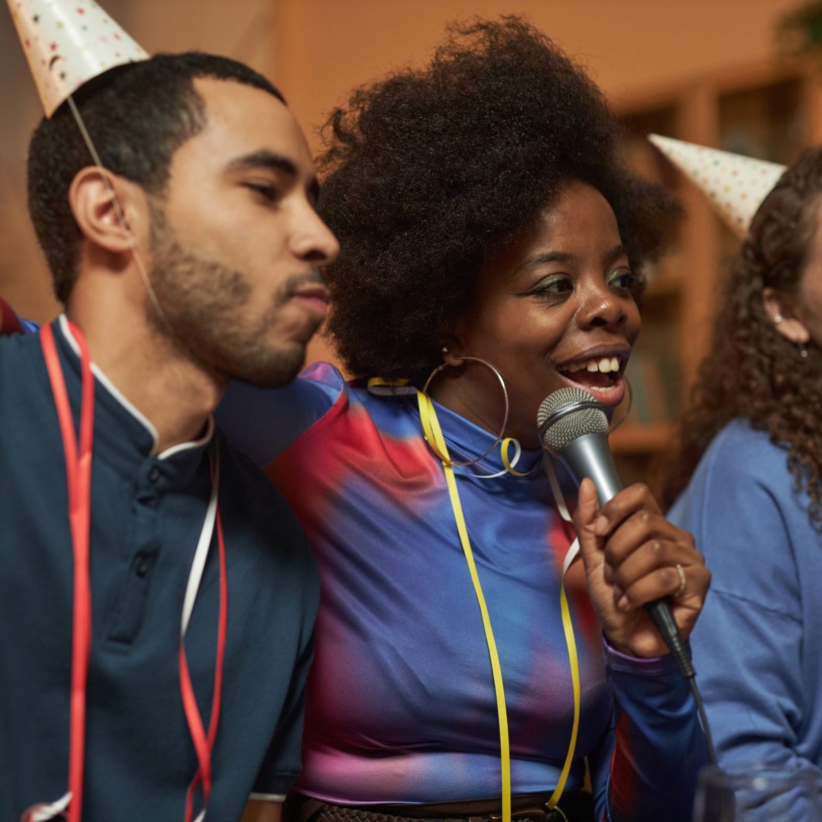 Multiethnic group of adult friends singing to microphone and enjoying karaoke during home party
